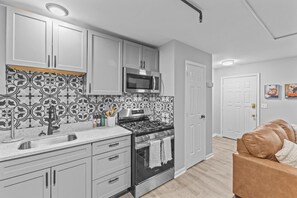 Una cucina moderna con mobili bianchi, una parete di fondo bianco e nero, elettrodomestici in acciaio inossidabile e un piano di lavoro in legno.