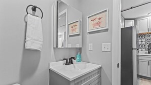Un baño con lavamanos blanco, espejo y perchero para toallas.
