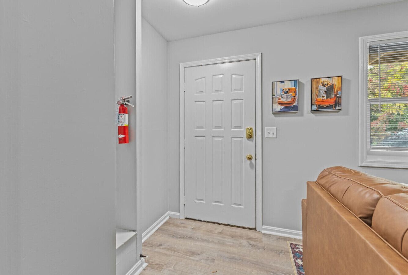 A hallway with a white door, a fire extinguisher, and a brown leather couch.