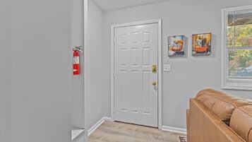 A hallway with a white door, a fire extinguisher, and a brown leather couch.