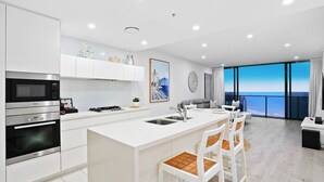 A modern kitchen with white cabinetry, a built-in oven, and a large island with bar stools. - Luxury Oracle Tower 2 Ocean Views 2BR Lvl33 (Broadbeach)