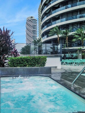 A modern hotel with a rooftop pool, surrounded by lush greenery and palm trees.