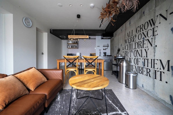 A modern living room with a brown leather sofa, a wooden coffee table, and a dining area with a wooden table and chairs.