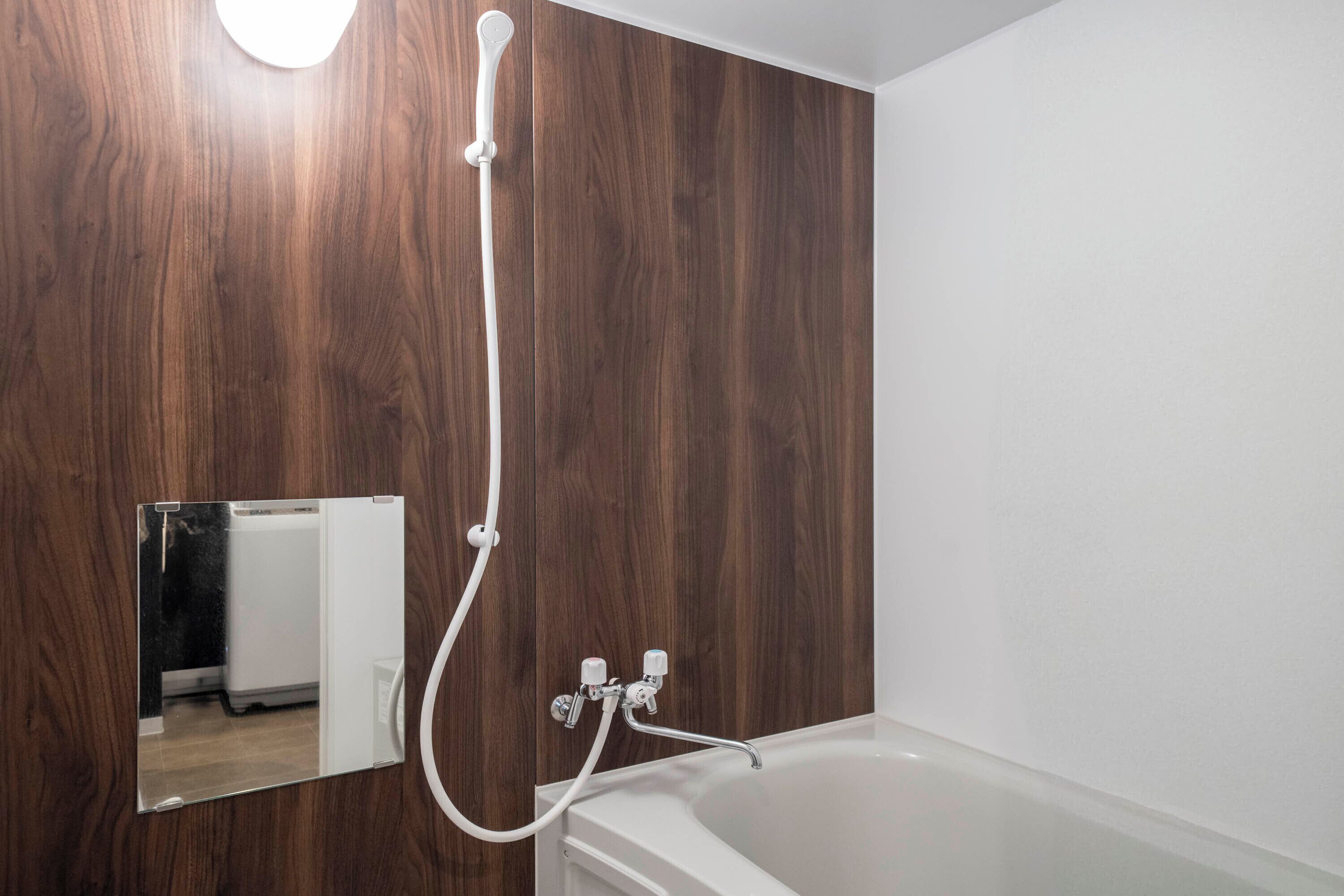 A bathroom with a wooden wall, a white bathtub, and a mirror reflecting a refrigerator.
