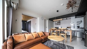 Un salon moderne avec un canapé en cuir marron, une table basse en bois et un coin cuisine comprenant une table à manger et des chaises.