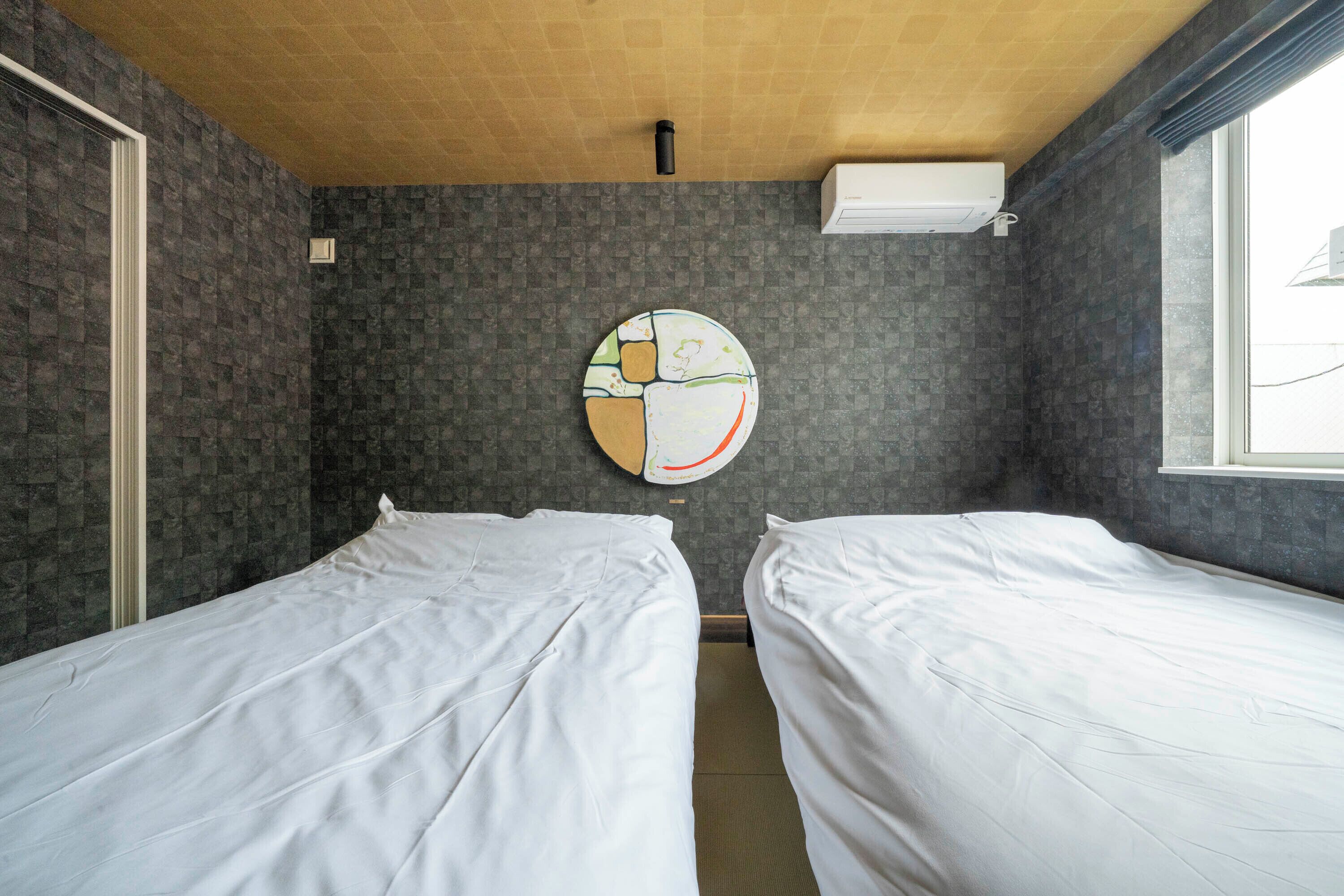 Une chambre d’hôtel avec deux lits simples, une horloge murale ronde et une fenêtre donnant sur un paysage agréable.