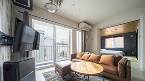 Un salon moderne doté d’un téléviseur à écran plat, d’un canapé en cuir, d’une table basse en bois et d’une grande fenêtre offrant une vue sur la ville.