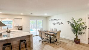 A modern kitchen with a central island, bar stools, a dining table with chairs, and a large potted plant. - 5-bedroom home in Port Charlotte (Port Charlotte)