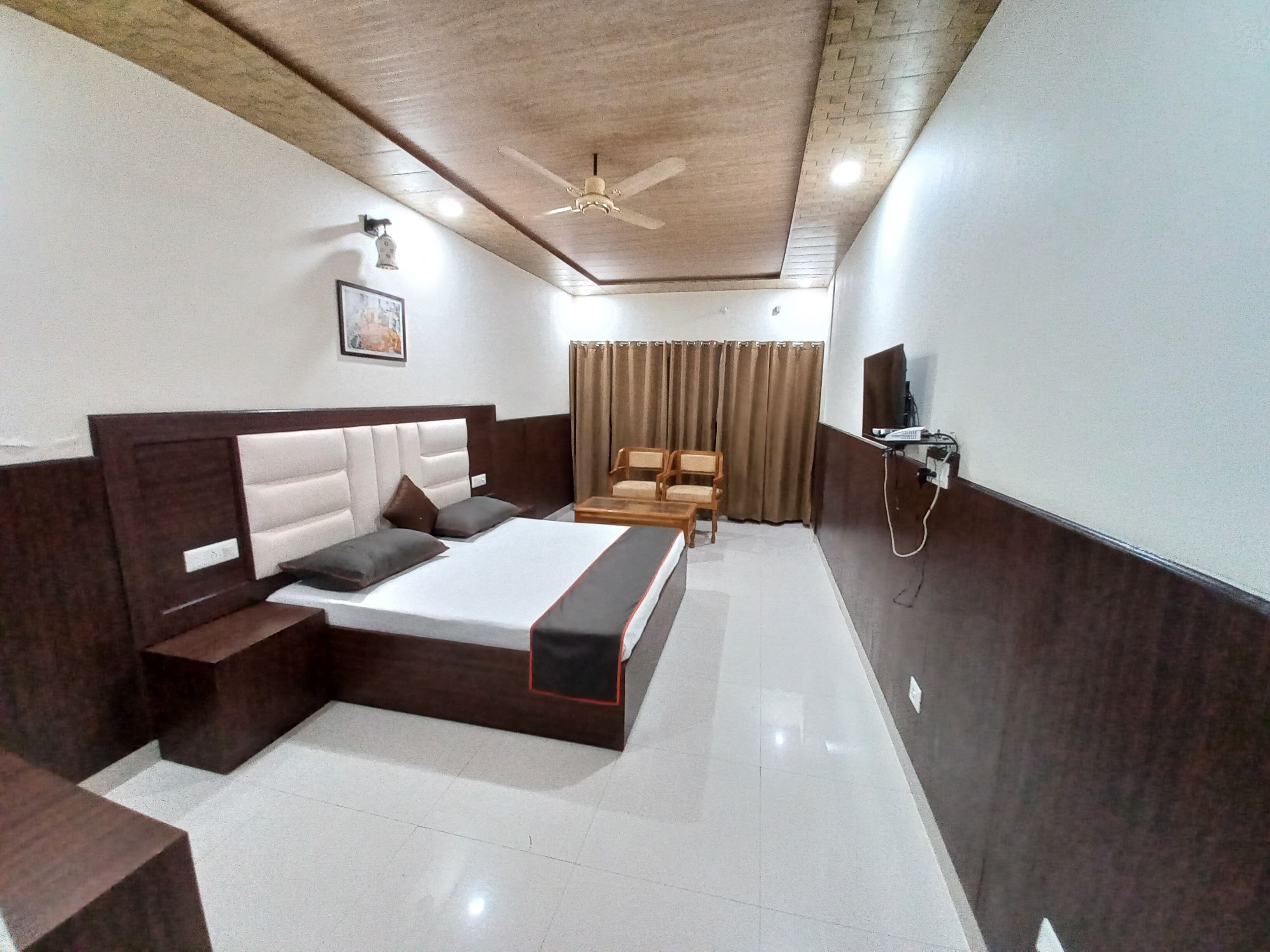 A modern hotel room with a large bed, a desk, a chair, a ceiling fan, and a television.