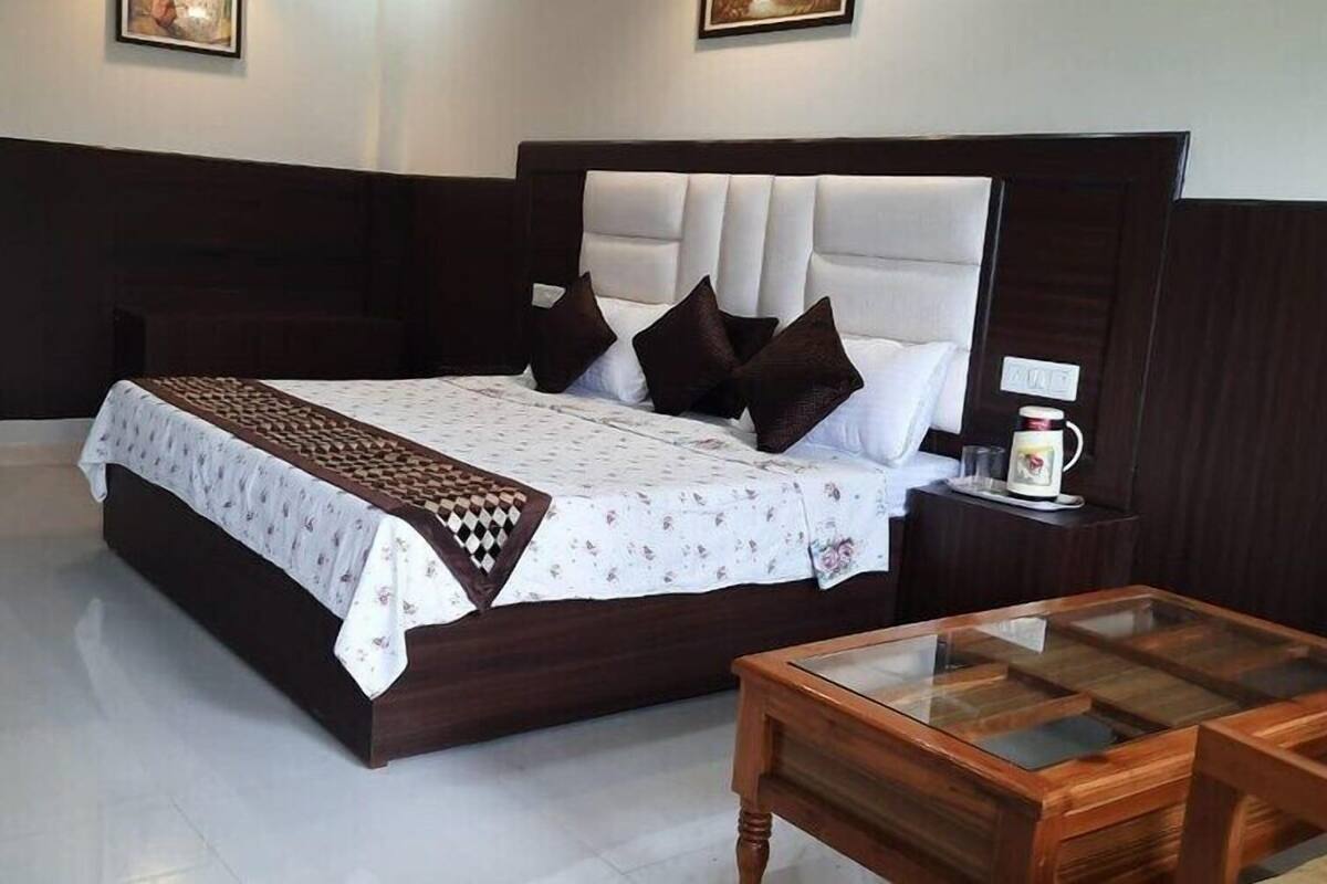 A neatly arranged hotel room with a large bed, a bedside table with a lamp, and a small wooden table.