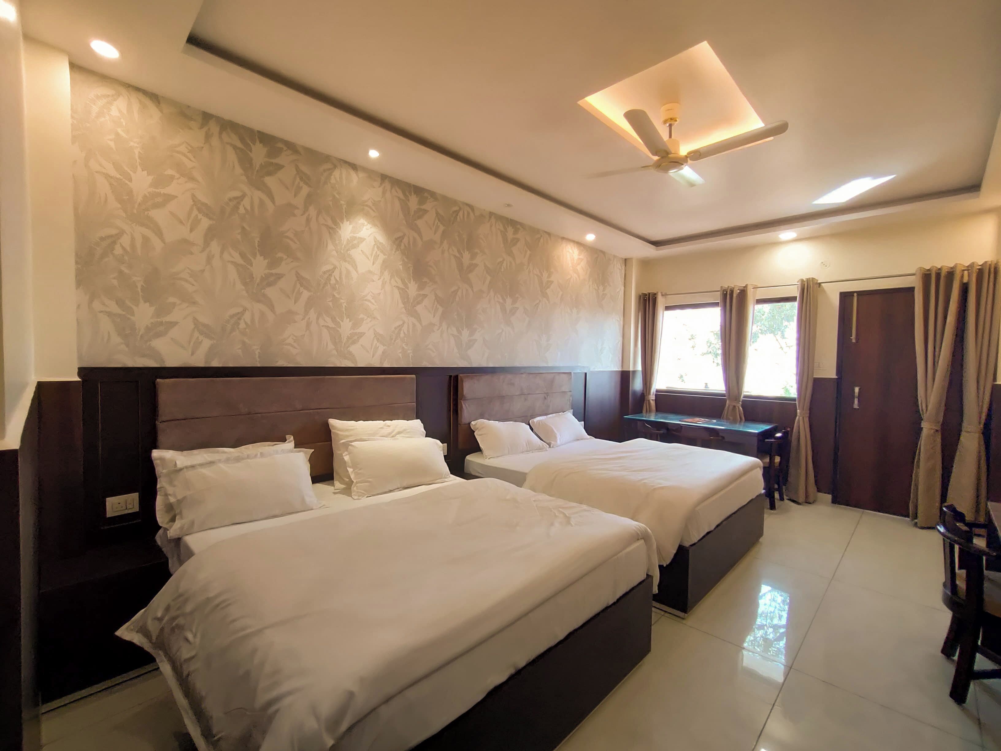 A hotel room with two beds, a desk, a chair, a ceiling fan, and a window with curtains.