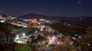 Vista nocturna de un pueblo con edificios iluminados, una colina al fondo y cielo despejado.