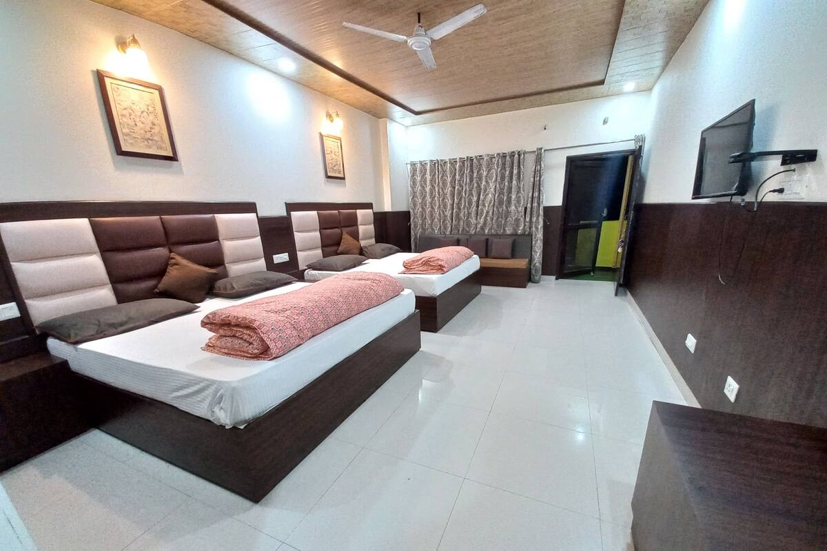 A hotel room with two beds, a sofa, a TV, and a ceiling fan.
