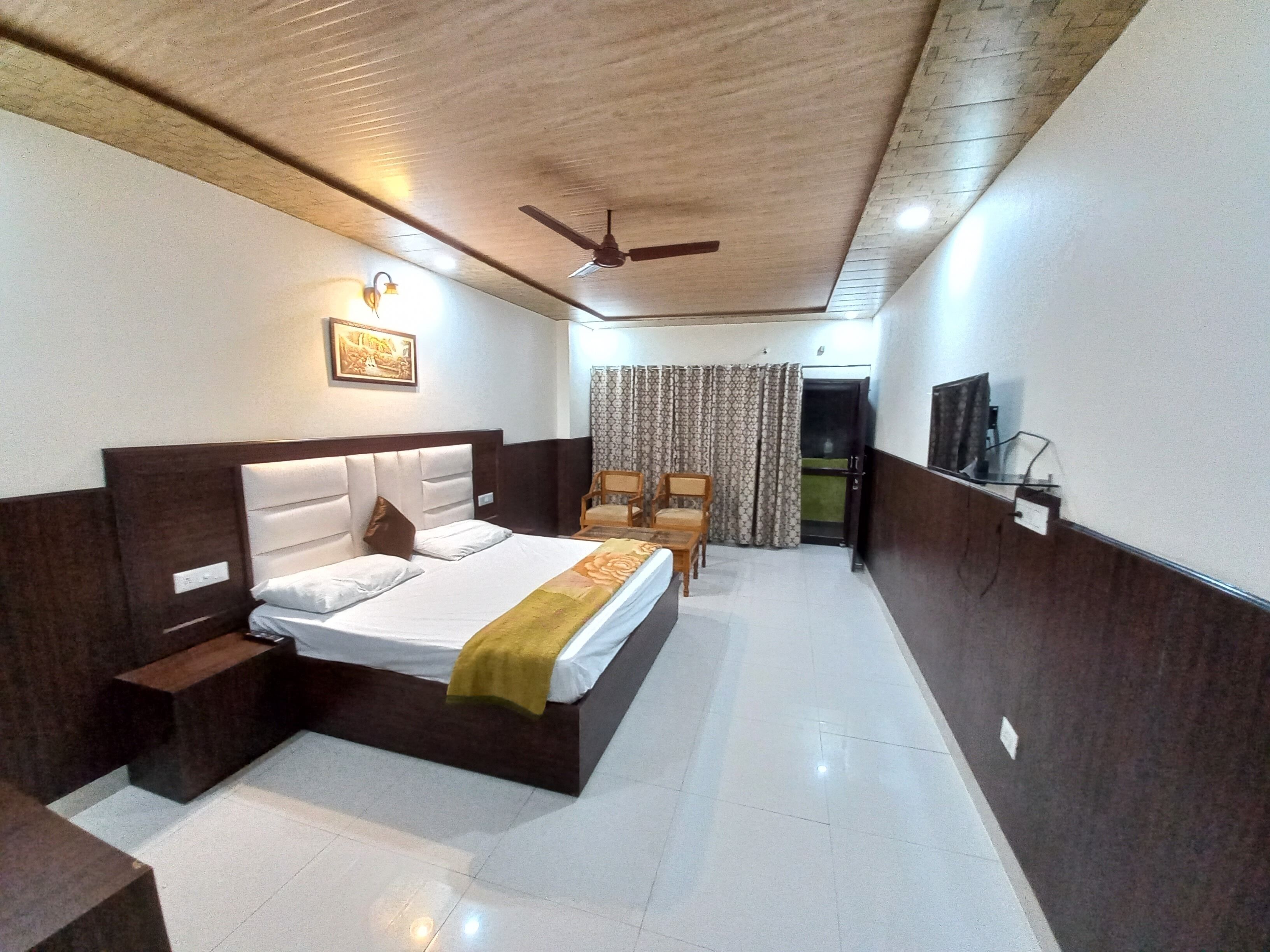 A hotel room with a bed, bedside tables, a ceiling fan, a TV, and a window with curtains.