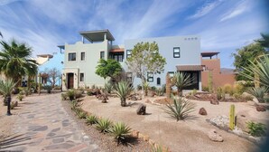 A modern building with a stone pathway leading to the entrance, surrounded by various cacti and desert plants. - Pristine 3-bed, 3.5-bath villa with mountain, golf course, sea views & hot tub 
 (Loreto)