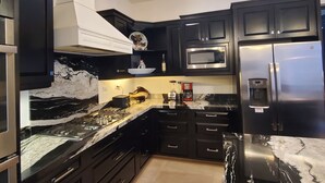 A modern kitchen with black cabinets, a marble countertop, stainless steel appliances, and a pendant light. - Pristine 3-bed, 3.5-bath villa with mountain, golf course, sea views & hot tub 
 (Loreto)
