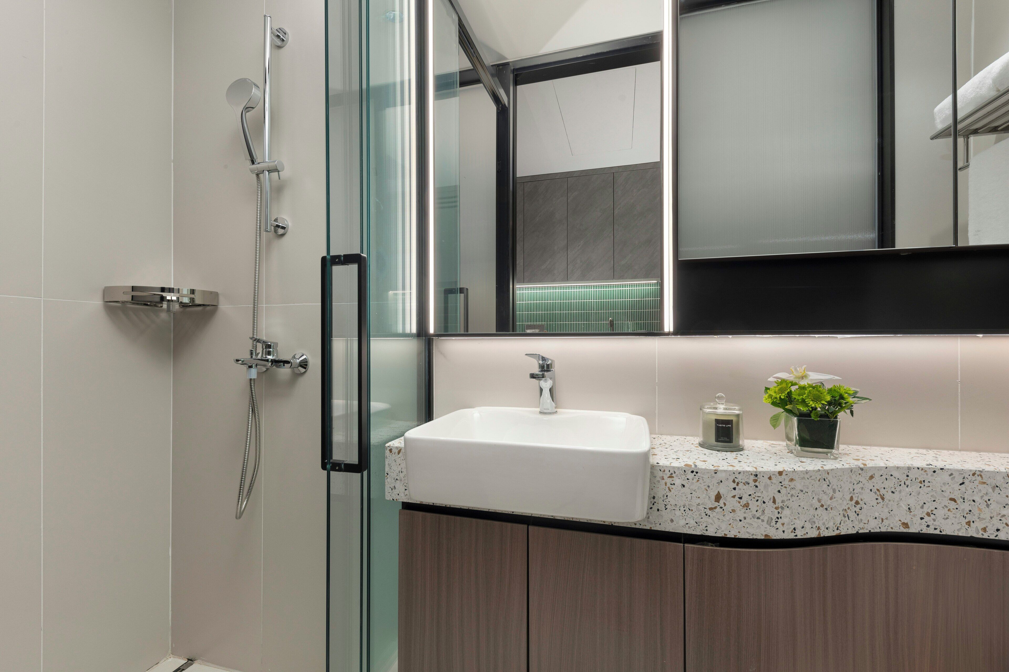 Une salle de bain moderne avec une douche à parois de verre, un lavabo blanc et un plan de toilette au motif moucheté.