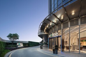 A modern hotel entrance with a curved facade, large windows, and a well-lit interior visible through the glass doors. - Modena By Freser Shenzhen (Shenzhen)