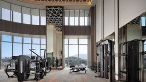 A gym with various exercise equipment, large windows, and a view of a cityscape. - Modena By Freser Shenzhen (Shenzhen)