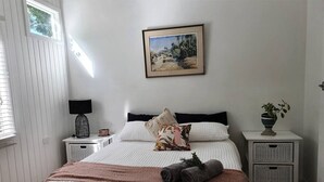 Une chambre à coucher bien rangée, avec un lit, des oreillers, une table de chevet avec une lampe, une petite table avec une plante et un tableau accroché au mur.