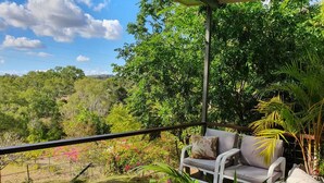 Un balcon agrémenté d’un canapé et de plantes, donnant sur un jardin luxuriant et des arbres.