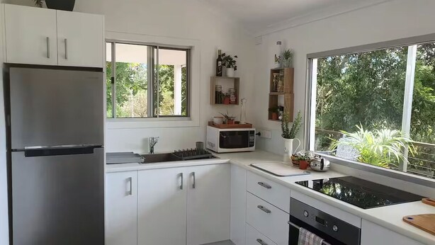 Une cuisine moderne avec des meubles blancs, un réfrigérateur en acier inoxydable, un four à micro-ondes et un lave-vaisselle. Une fenêtre offre une vue sur la verdure environnante.