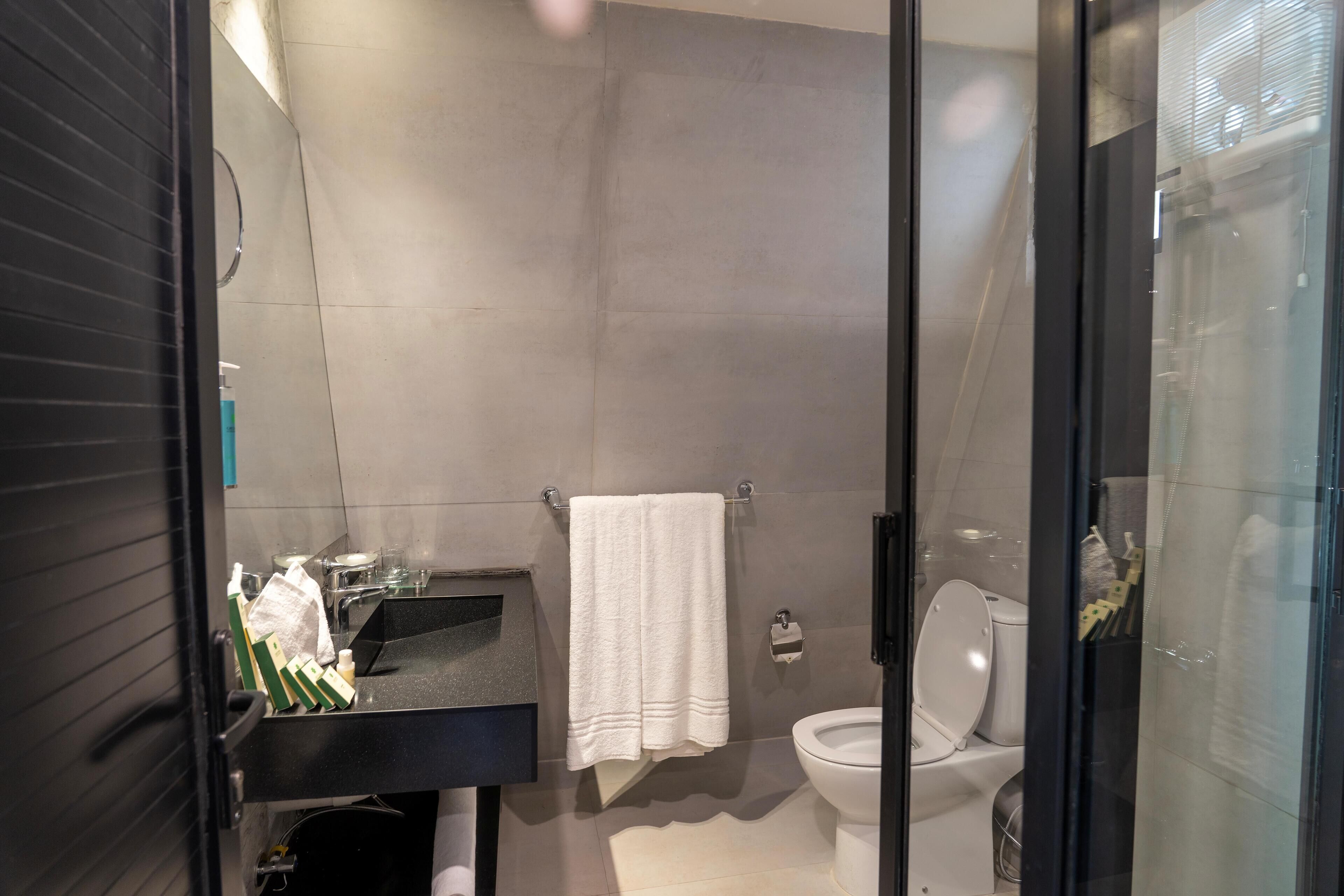 Un baño moderno con un lavamanos negro, una toalla blanca y una cabina de ducha con mampara de vidrio.