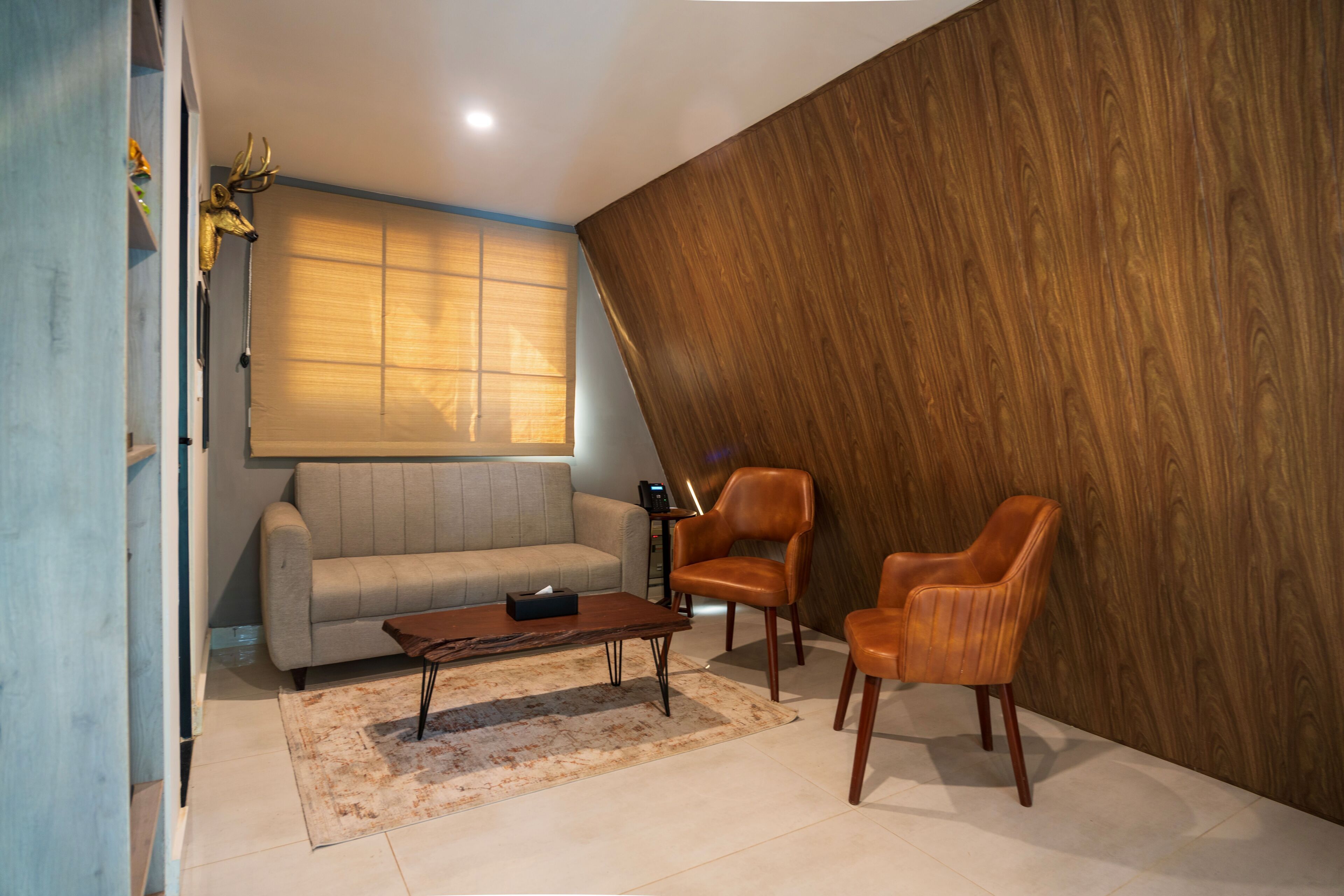 A modern living room with a sofa, two leather chairs, a coffee table, and a wooden accent wall.
