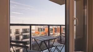 Un balcón con vistas a edificios urbanos, una mesa de madera y una silla.