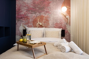 A bedroom with a bed, pillows, a bedside table with a tray, a lamp, and a wall mural.