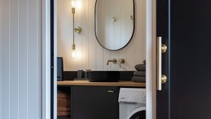 A modern bathroom with a black sink, a mirror, and a washing machine.