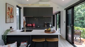 A modern kitchen with a large island, dark cabinetry, and a view of the outdoors.