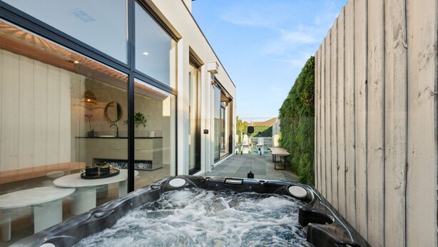 A spa area with a hot tub, a glass-enclosed bathroom, and a patio with outdoor seating. - Bayside Grandeur with Heated Pool, Spa and Sauna plus each Bedroom has Ensuite (Bentleigh)