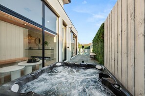 Un área de spa con un jacuzzi, un baño con paredes de vidrio y una terraza con mobiliario exterior.