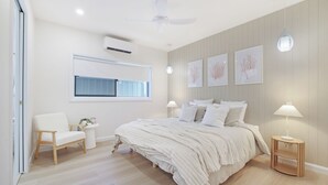 Een slaapkamer met een bed, nachtkastjes, een stoel, een raam en wanddecoratie.