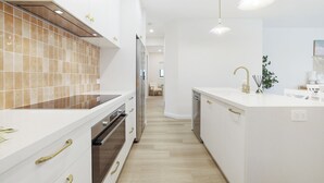 Een moderne keuken met witte kasten, een centraal eiland en een houten spatwand.