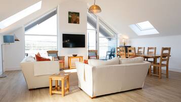 Relax in this spacious living area with a high ceiling and skylights, featuring a sofa, armchair, and flat-screen TV.