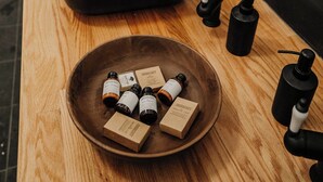 Un plan de travail en bois, surmonté d’un évier noir, d’un miroir et d’un récipient contenant de petits flacons et des boîtes.