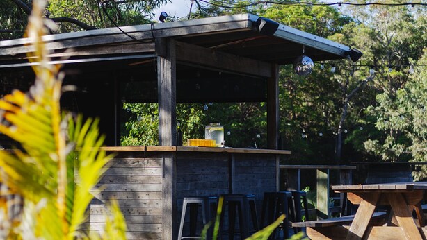Un espace bar extérieur en bois, au design rustique, comprenant un comptoir, des tabourets et une grande table en bois.