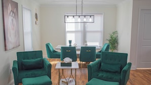 A dining area with a white table, green upholstered chairs, and a chandelier.