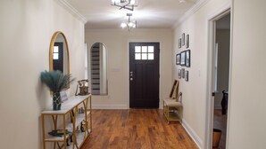 A hallway with wooden flooring, a black door, a mirror, and a console table with decorative items.