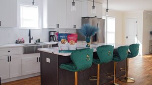 A modern kitchen with white cabinets, a stainless steel sink, and a central island with green bar stools.