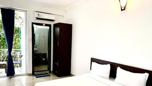 Une chambre d’hôtel comprenant un lit, une armoire, une salle de bain avec douche et un balcon avec des rideaux.