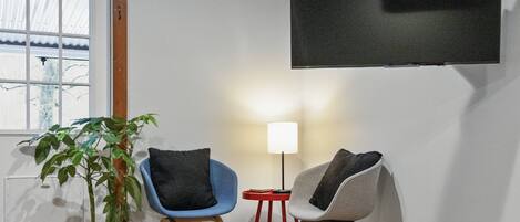 Une pièce avec un téléviseur fixé au mur, deux chaises, une petite table avec une lampe et une plante en pot.