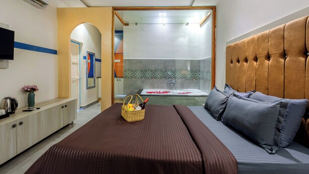 Ein Hotelzimmer mit einem Bett, einem Nachttisch mit Lampe, einem an der Wand befestigten Fernseher und einem durch eine Glastür einsehbaren Badezimmer.