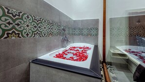 Ein modernes Badezimmer mit einer Badewanne voller Rosenblätter, einer Duschkabine und dekorativen Wandfliesen.