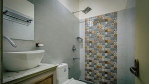 Ein Badezimmer mit einem großen, weißen Waschbecken, einer Toilette, einer Dusche mit gefliestem Wandbereich und einem Handtuchhalter.