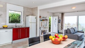 A modern kitchen with red cabinets, a white refrigerator, and a dining area with a glass table and chairs. - Mon Coeur by Interhome (El Port de la Selva)