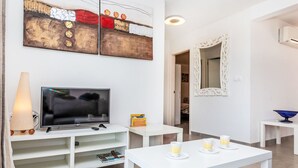 A modern living room with a flat-screen TV, white furniture, and a decorative wall piece. - Mon Coeur by Interhome (El Port de la Selva)