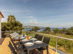 Un área de comedor al aire libre con una mesa lista para cuatro, con vistas panorámicas del mar y las montañas.